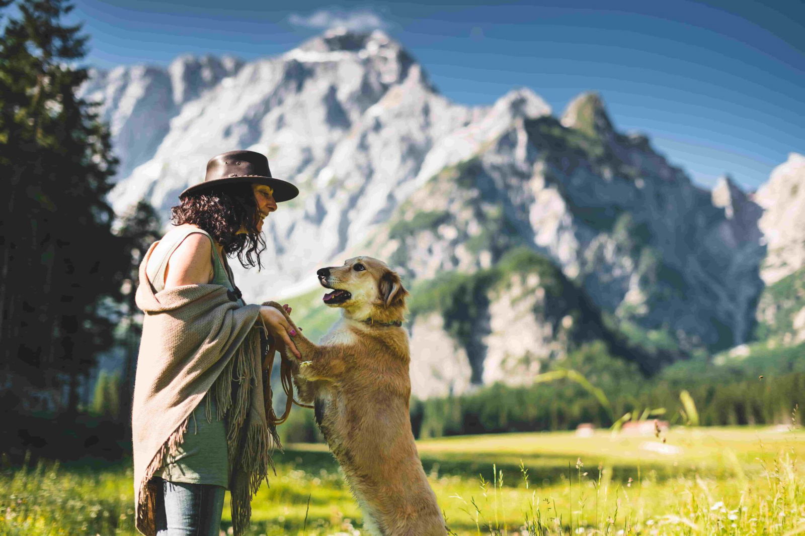 Eine Frau und ihr Hund stehen vor einer Bergkulisse.