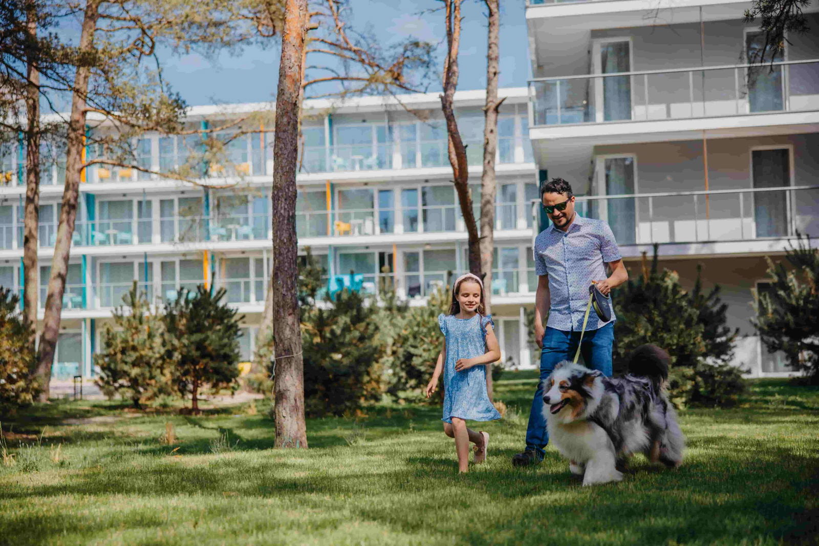 Mann und Kind spazieren mit Hund auf den Grünflächen rund um das Linea Mare Resort.