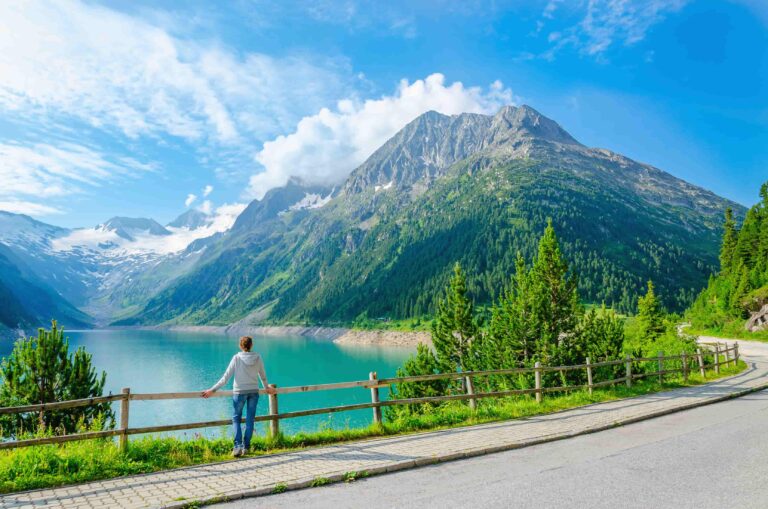 Eine Frau steht an einem Zaun mit Blick auf einen See und die Berge.