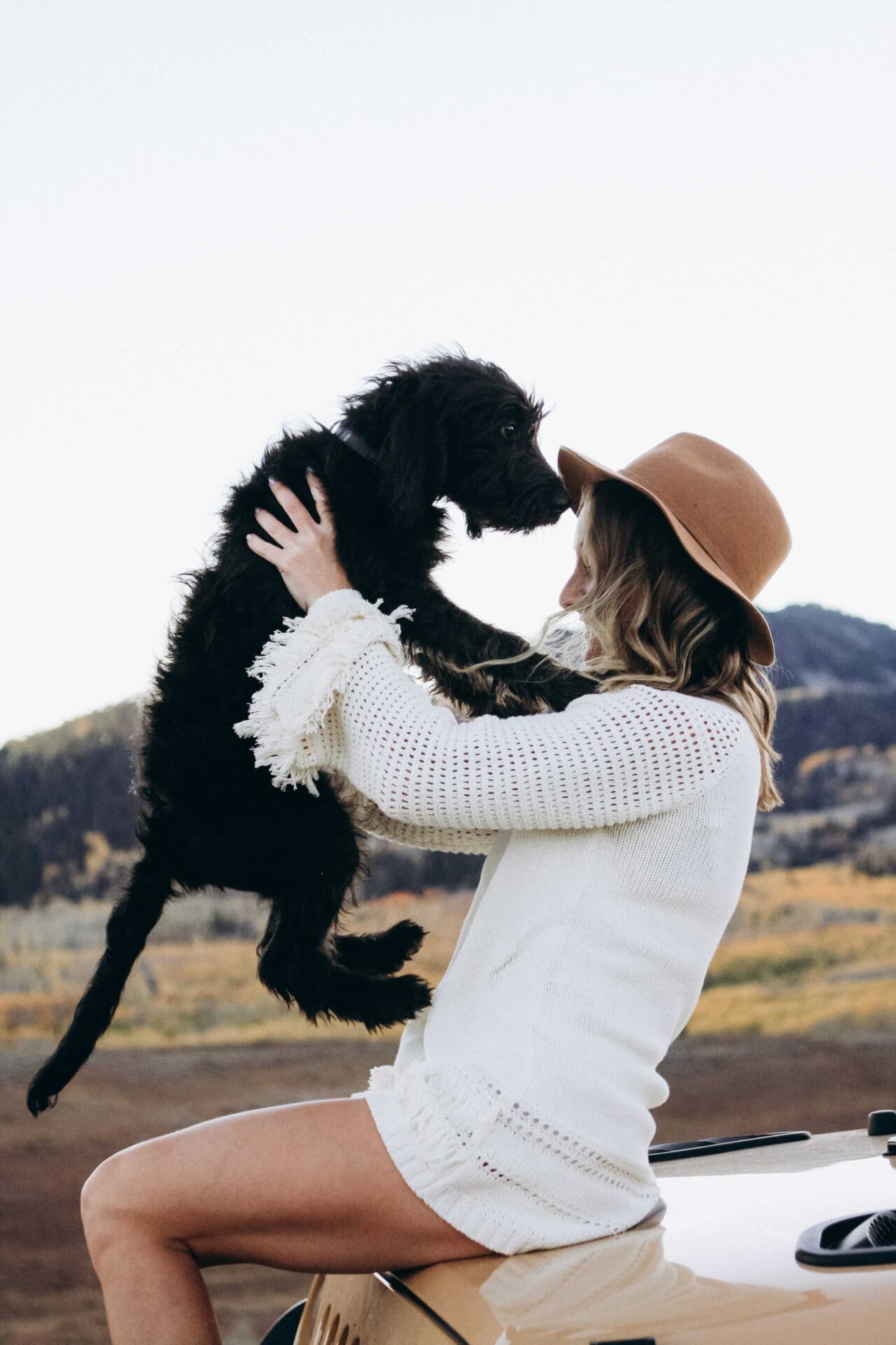 Eine Frau mit Hut hält einen schwarzen Hund in die Höhe.